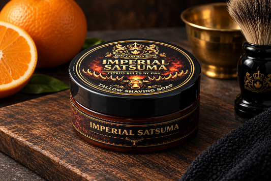A tub of Imperial Satsuma  Shaving Soap by First Canadian Shave sits on a rustic wooden cutting board, surrounded by shaving props including an orange, a brass bowl, a shaving brush, and a dark towel.