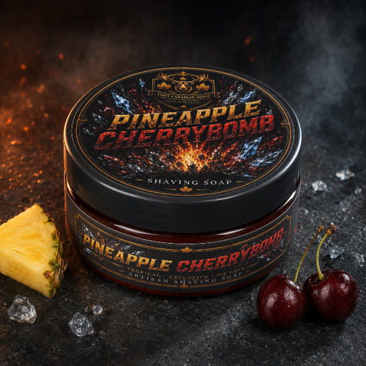 A tub of Pineapple Cherrybomb Shaving Soap by Canadian Shaving Soap, styled on a dark textured surface with a slice of pineapple, cherries, and ice crystals. The product features a black lid with a fiery orange and yellow graphic, and a dark brown body.