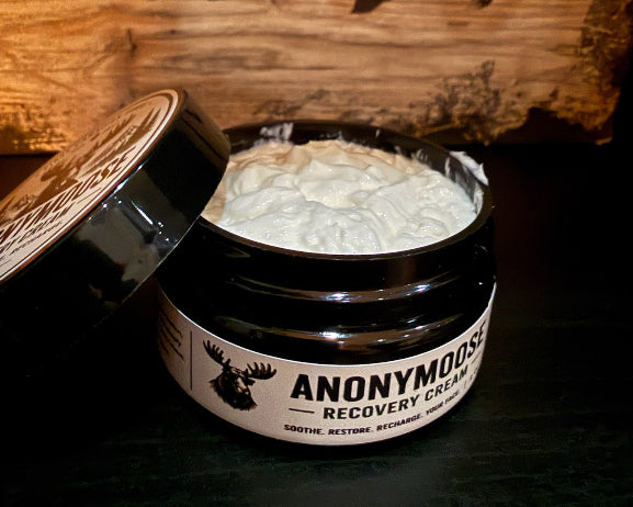 An open  jar of Anonymous Recovery Cream by First Canadian Shave showing the white cream inside, set against a rustic wooden background.