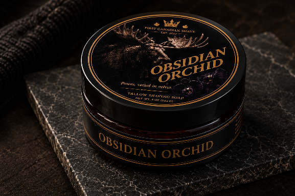 A tub of Obsidian Orchid shaving soap by First Canadian Shave, placed on a dark stone slab with a dark textured towel in the background.